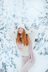 Beautiful young girl posing in the winter in cold snowy forest with pine trees.