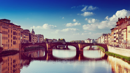 View from the river to the famous italian medieval bridge - Ponte Vecchio in Florence with blue sky and clouds, travel outdoor Italy sightseeing background