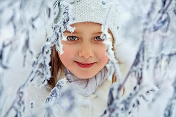 Happy adorable child girl in fur hat and coat in winter forest