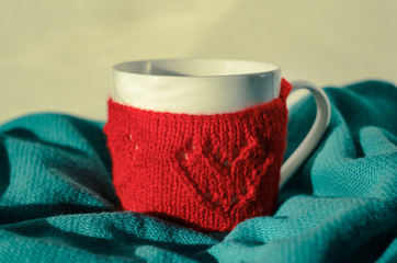 Still life of Cozy Mug in red knitted mitten with heart pattern on mint color background. Retro Look