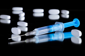 syringe and medical pills on a black reflective surface, needle and drugs