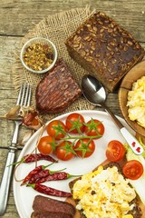 Scrambled eggs with bread and salami. Egg breakfast on a wooden table. Healthy food.