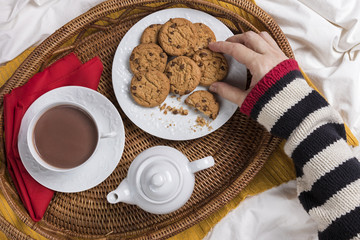 Breakfast in bed / Tray with hot chocolate and cookies with female hand holding a cookie, top view