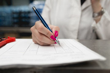 Close up shots of nicely manicured woman hands writing something in water bottling factory production line. Blurred canisters and galons in background.