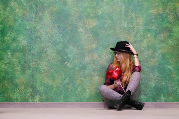 Closeup portrait girl with red balloons with heart shape on a green background. Horizontal shot . Girl hipster in a black hat holding a red inflatable heart and celebrate Valentine's day.