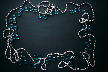 Fototapeta na wymiar Frame of silver beads and blue glass pebbles on a black background