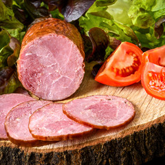 Sausage, ham with tomatoes and lettuce on a wooden board, stump