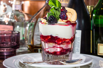 A dessert of fresh yoghurt, jam and fresh berries in a glass.