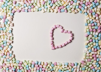 Heart in the frame of colorful mini marshmallows on white background. Top view