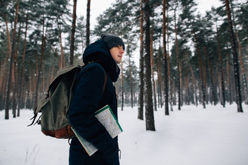 Fototapeta na wymiar Traveler in winter clothes with travel rucksack and map walking in forest. Travel concept