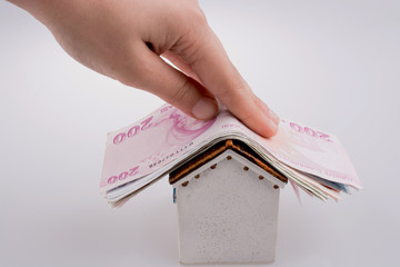 Hand holding Turkish Lira banknotes on the roof of a model house