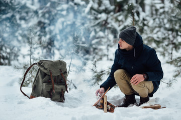Fototapeta na wymiar Man kindle bonfire in winter forest in snowy weather. Travel concept