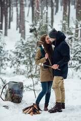 Сouple in love near the fire heated in winter forest. Travel concept