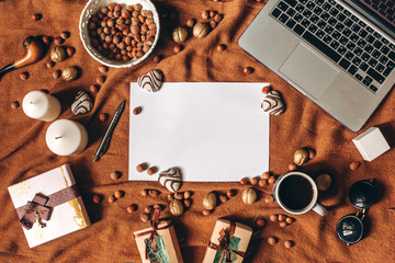 Home workspace in romantic style with laptop, notebook, heart shaped biscuit, pen, coffee cup, gifts, nuts on brown fabric cover. Empty sheet in center. Copyspace, top view, flat lay
