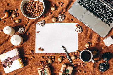 Home workspace in romantic style with laptop, notebook, heart shaped biscuit, pen, coffee cup, gifts, nuts on brown fabric cover. Empty sheet in center. Copyspace, top view, flat lay