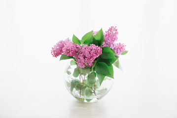 bouquet of lilac in round transparent vase near window