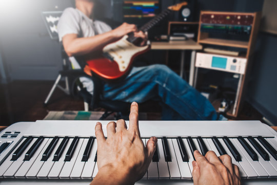 music jamming in sound studio, pianist hands playing keyboard on blurred guitar player background. film filter
