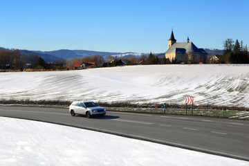 Krajobraz zimowy w górach, kościół, samochód osobowy na drodze.