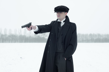 Retro 1920s english gangster with black coat and flat cap shooti