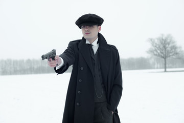 Retro 1920s english gangster with black coat and flat cap shooti