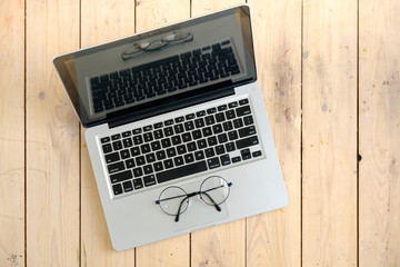 Laptop and glasses on wooden desk, top view