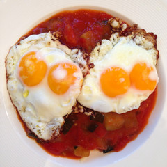 Two double yolk fried eggs on vegtetable ratatouille served in a white dish. Mobilestock