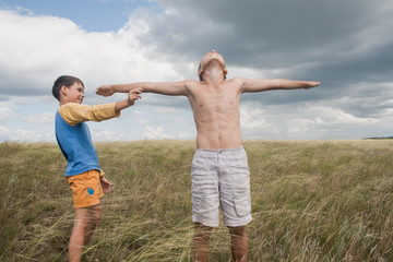 young boys playing in a field. boys in shorts. Boys stand in the desert. feather in the field. boy looking up at the sky. dreamer. two brothers. two friends. children playing in the field.
