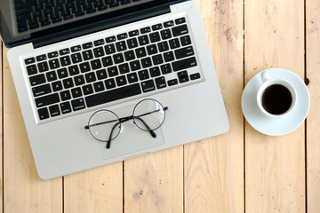 Laptop, glasses and coffee cup on wooden desk, top view