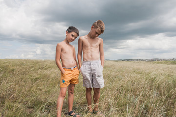 young boys standing in a field. boys in shorts. Boys stand in the desert. feather in the field. boy looking up at the sky. dreamer. two brothers. two friends. children playing in the field.
