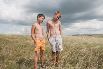 young boys standing in a field. boys in shorts. Boys stand in the desert. feather in the field. boy looking up at the sky. dreamer. two brothers. two friends. children playing in the field.