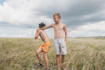 young boys playing in a field.  boys in shorts. Boys stand in the desert. feather in the field. boy looking up at the sky. dreamer. two brothers. two friends. children playing in the field.