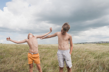 young boys playing in a field.  boys in shorts. Boys stand in the desert. feather in the field. boy looking up at the sky. dreamer. two brothers. two friends. children playing in the field.
