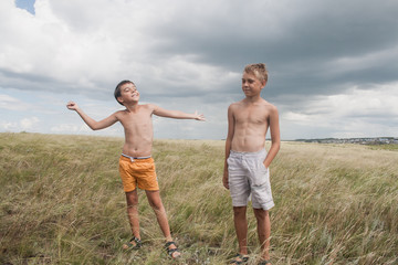 young boys standing in a field. boys in shorts. Boys stand in the desert. feather in the field. boy looking up at the sky. dreamer. two brothers. two friends. children playing in the field.