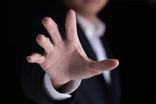 A business man in casual black suit gesturing  his palm hand against the camera.