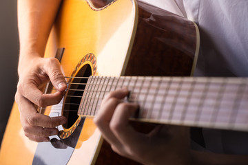 A man sitting and playing classic wooden guitar close up to chord tab fretboard.