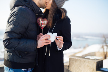 Beautiful young couple in love enjoying together at city street and holding together a  heart shape made from snow. 