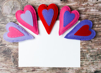 Hand made felt colorful hearts white paper on wooden background