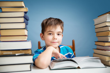 seven years old child reading a book at home. Boy studing at table on blue background