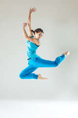 Fototapeta na wymiar Young beautiful slim girl in blue dancing on a white studio background