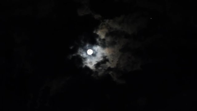  Noche de luna llena con fuerte resplandor de  la luna entre nubes y una estrella titilando
