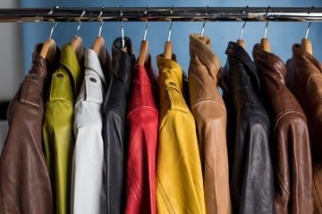 Different color leather jacket hanging on rack on blue background