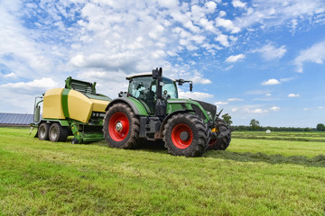 Ernte - Traktor mit Rundballenpresse im Einsatz für Grasssilage - obrazy, fototapety, plakaty