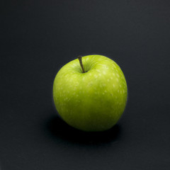 Single green apple on black background.