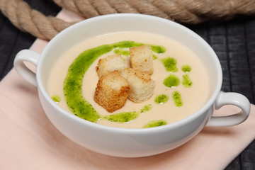 Creamy soup puree in white bowl and small pieces of fried bread