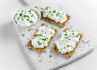 Homemade Crispbread toast with Cottage Cheese and parsley on white wooden board.