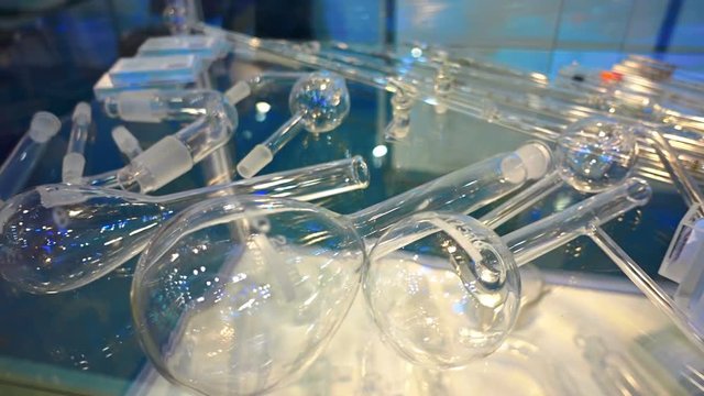 New glassware and other accessories for the chemical, medical and other activities on a glass showcase is reflected in the light. Shot in motion
