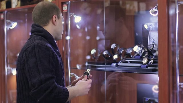 Young Man chooses wrist watch in the watch store