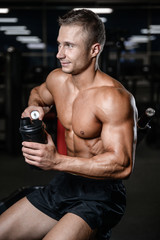 Fototapeta na wymiar Handsome fitness model holding a shaker in the gym gain muscle.