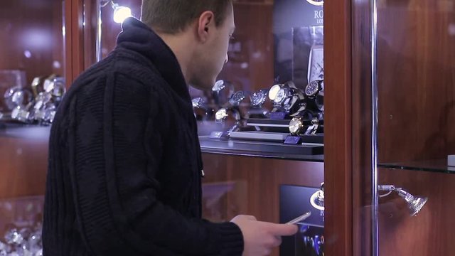 Young Man chooses wrist watch in the watch store using smartphone