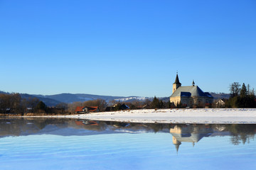 Kościół w górach zimą z odbiciem w wodzie jeziora.